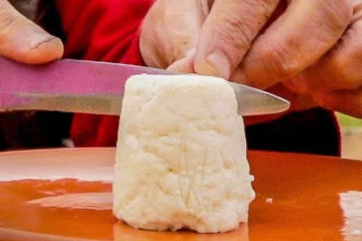 una mano taglia un pezzo di formaggio pule