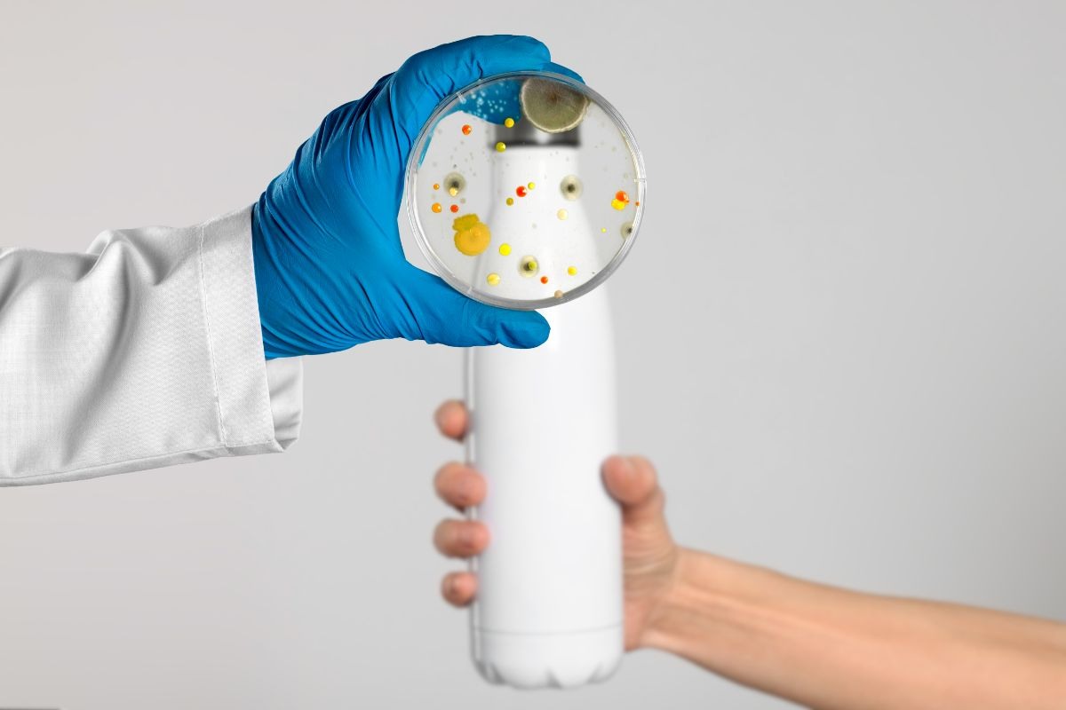 mano che mantiene borraccia e mano medica con un vetrino pieno di batteri