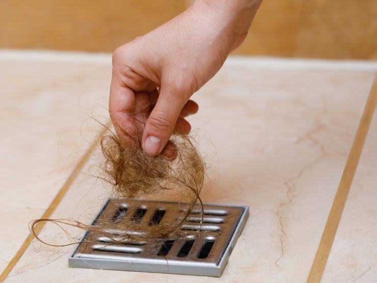 mano che toglie capelli dallo scarico della doccia