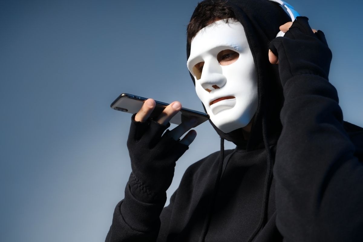 truffatore con una maschera che parla ad uno smartphone