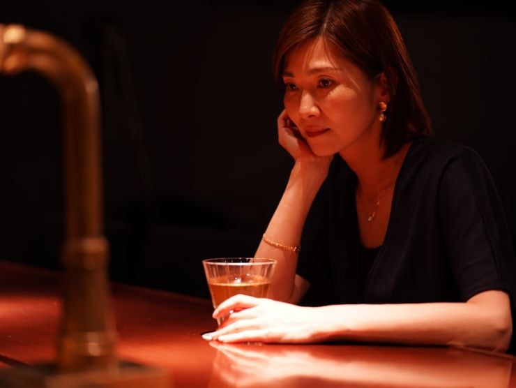 donna sola seduta al bancone del bar con un drink tra le mani