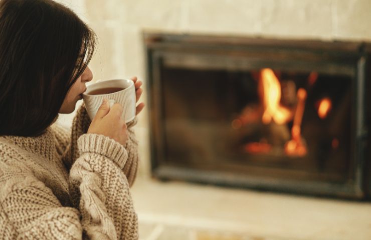 donna che beve bevanda calda di fronte ad un camino